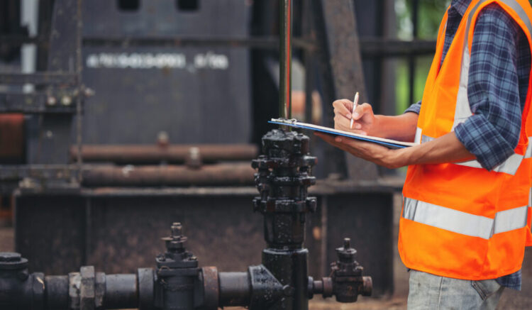 Workers standing and checking beside working oil pumps.